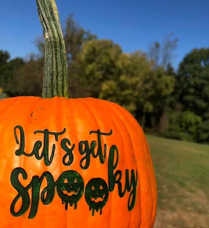 A pumpkin laser-engraved with the script words Let’s get spooky, outdoors under a blue sky