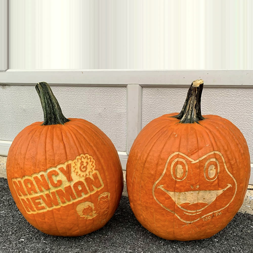 Two pumpkins side by side, one laser-engraved with the Nancy and Newman radio show logo and one with the Froggy 100.1 FM frog